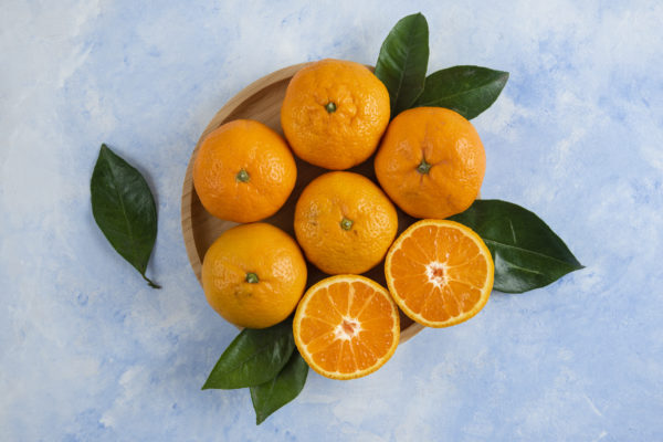 Top view of clementine mandarins with leaves on wooden plate